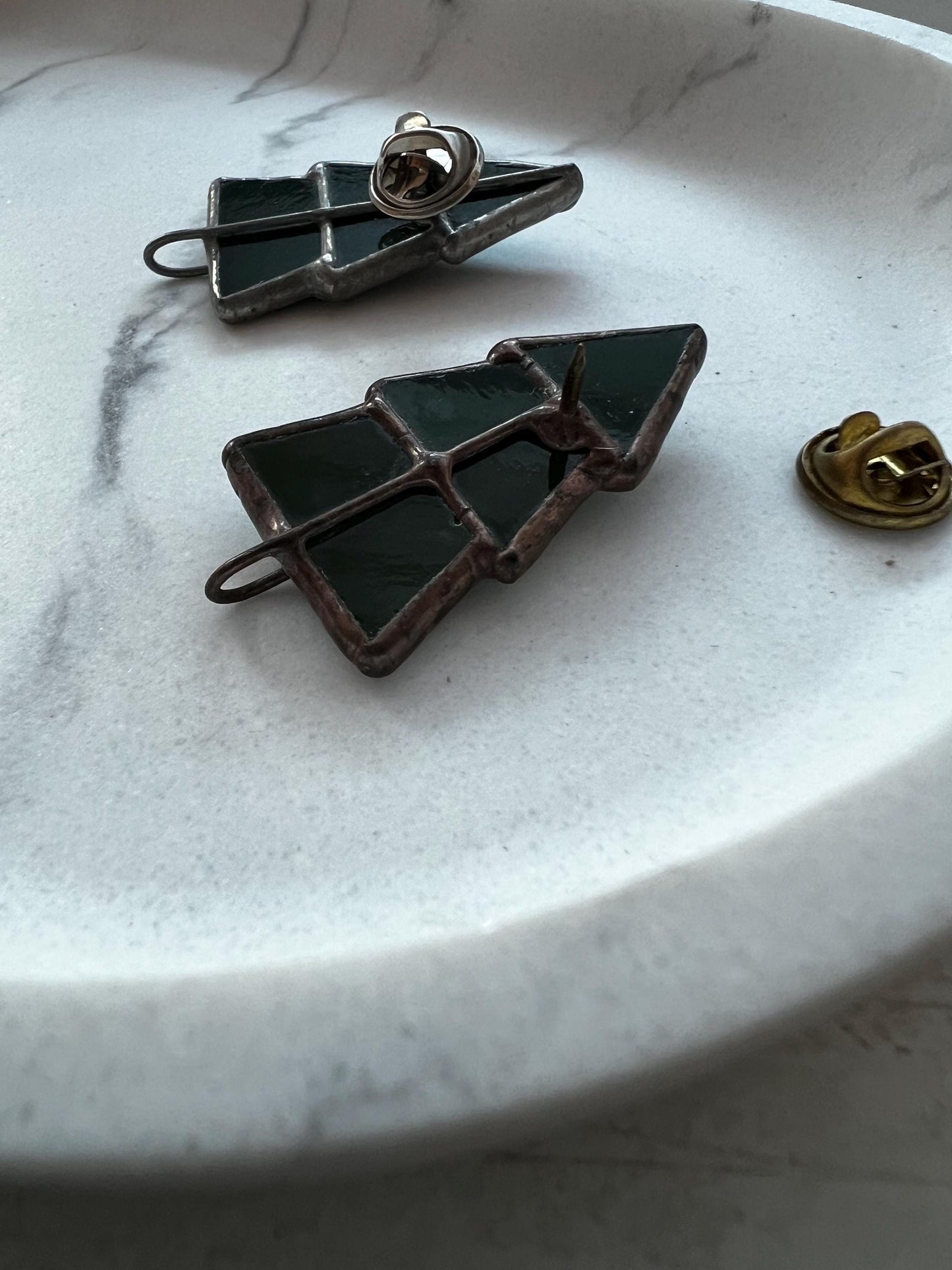 Back view of a stained glass Christmas tree brooch, demonstrating the attachment, lying on a light background