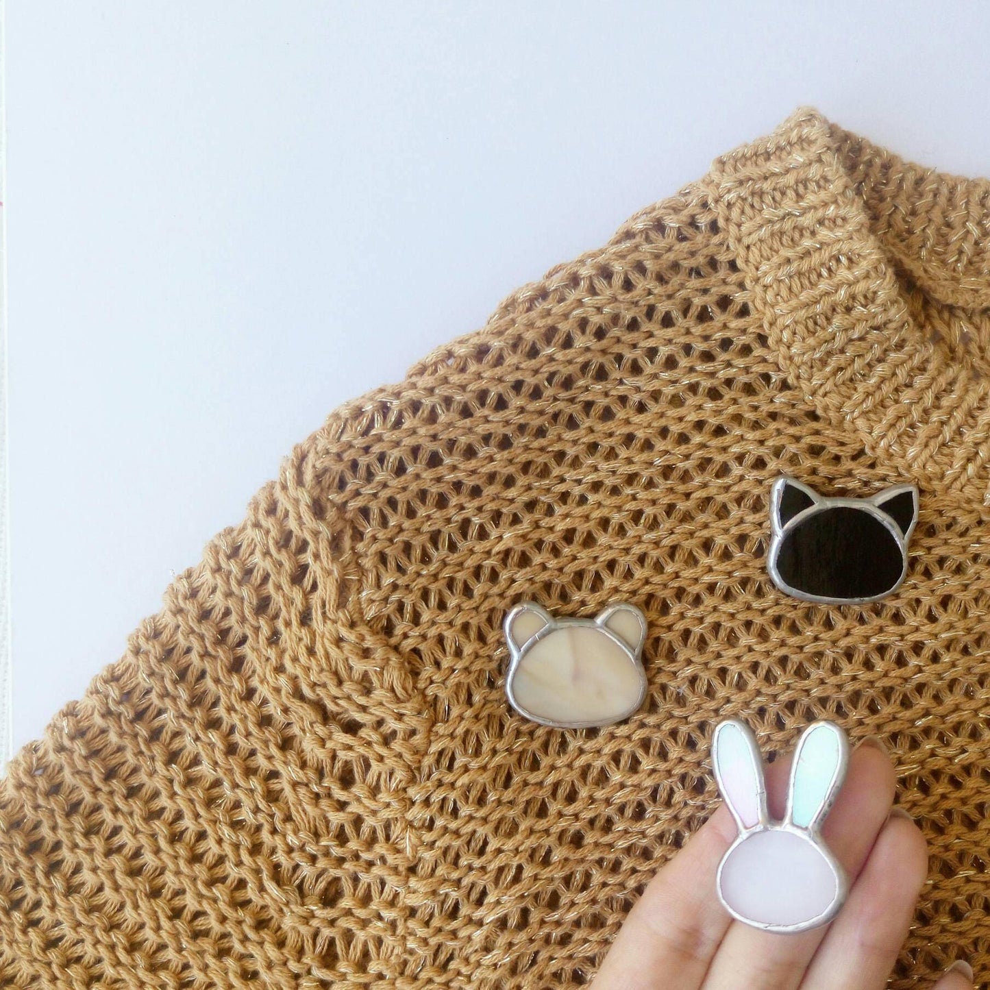 The photo shows three cute stained glass brooches in the shape of a teddy bear, a cat, and a bunny, pinned to a sweater.