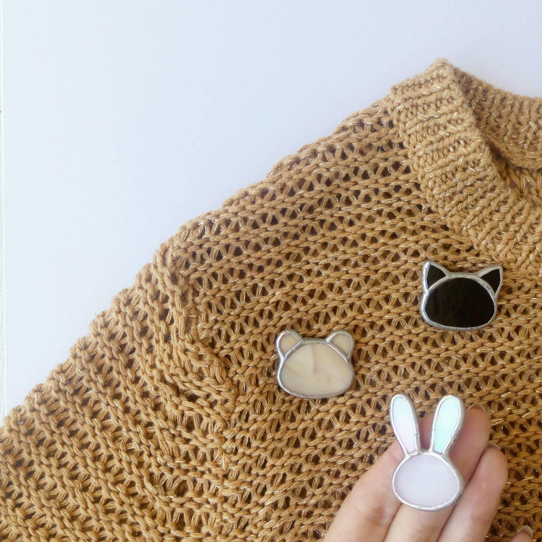 The photo shows three cute stained glass brooches in the shape of a teddy bear, a cat, and a bunny, pinned to a sweater.