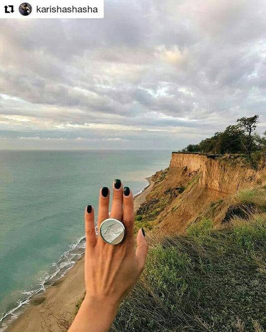 Large cocktail ring-mirror on the hand with a view of the rocks and the sea