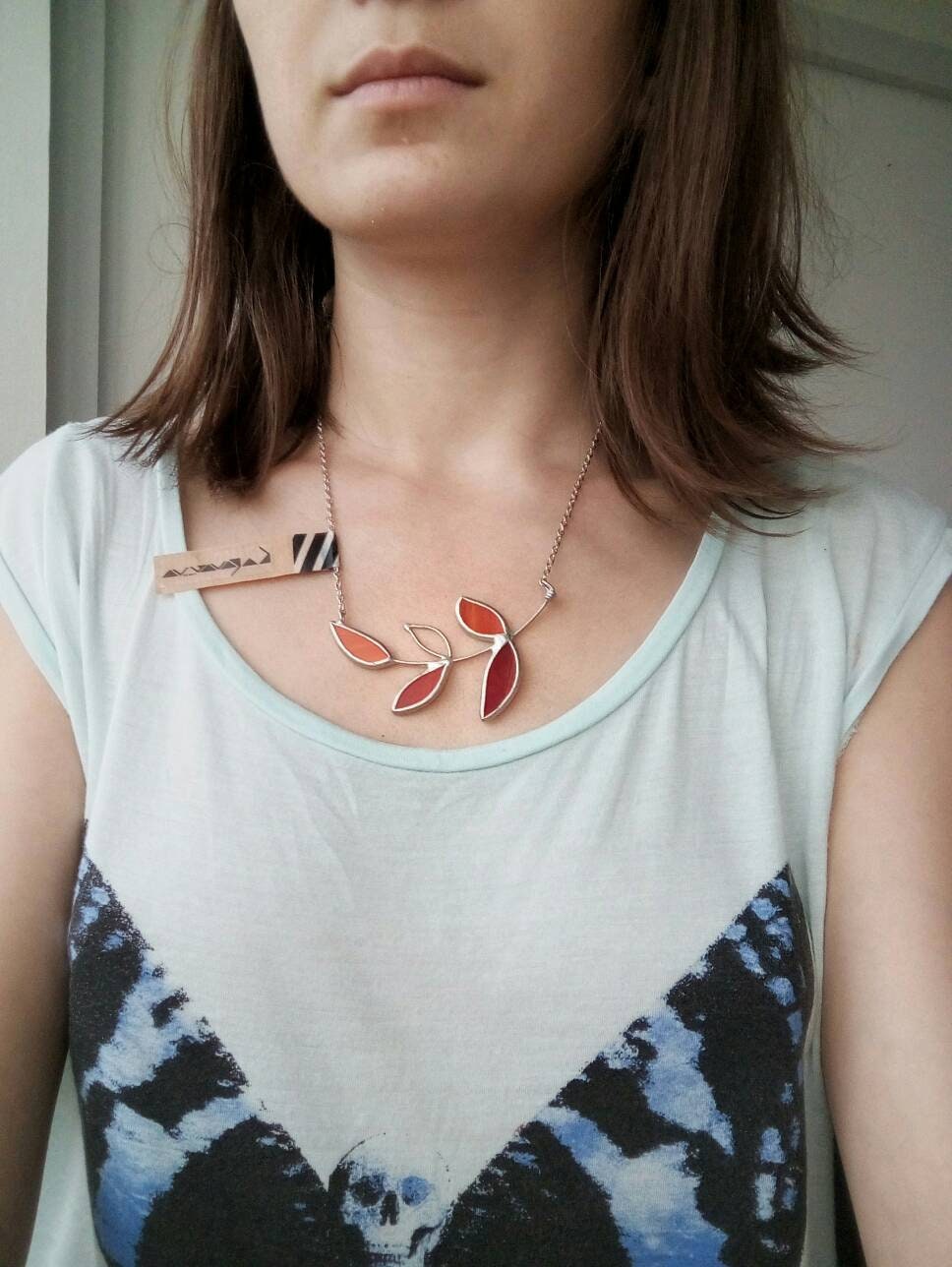 Handmade stained glass necklace with red and orange leaves on silver chain, botanical fall jewelry photographed on woman.