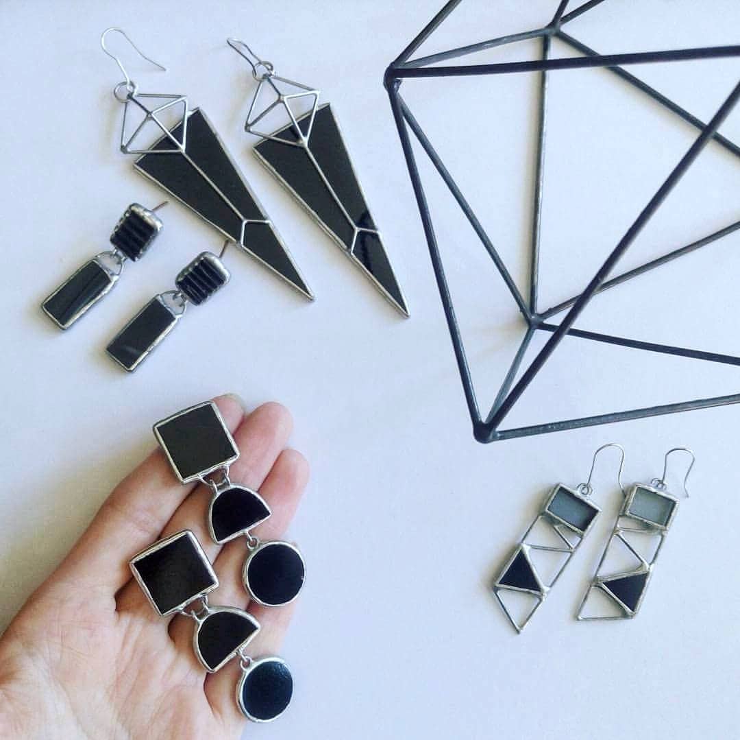 Collection of geometric glass earrings on a white background next to a decorative figure.