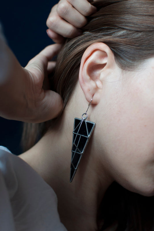Close-up of black geometric triangle stained glass earrings worn on ear