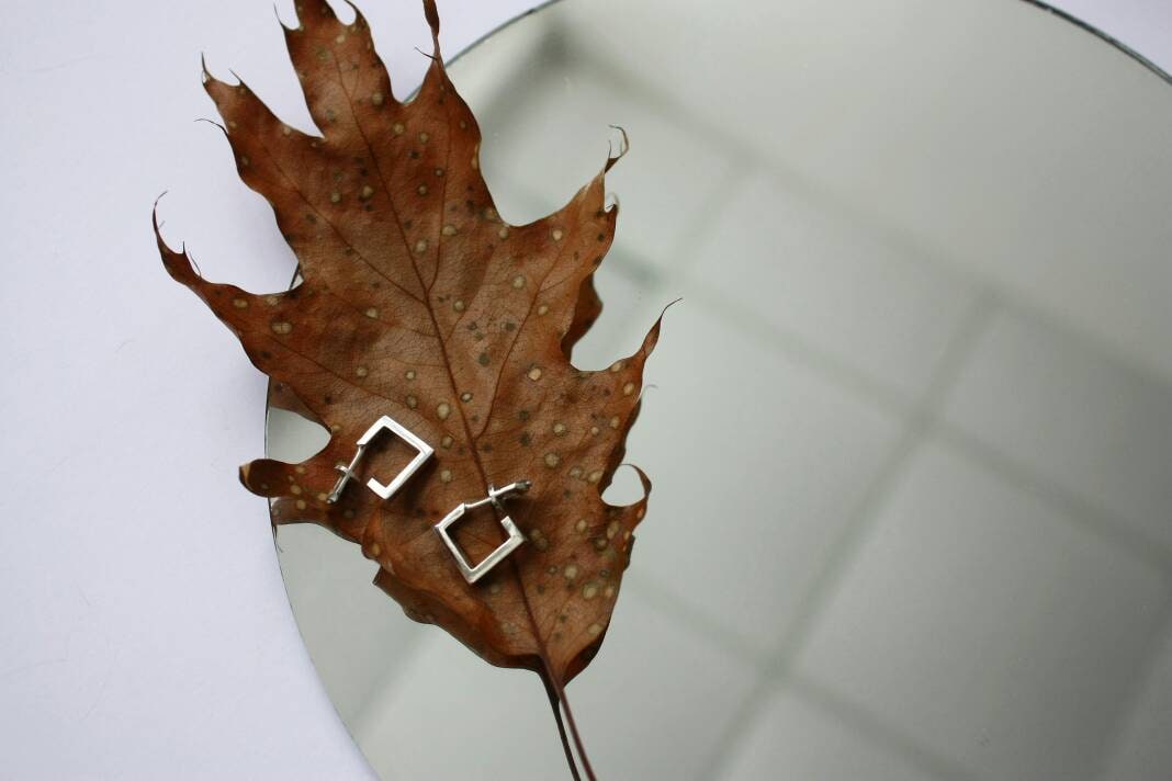 Small square earrings lying on an autumn leaf