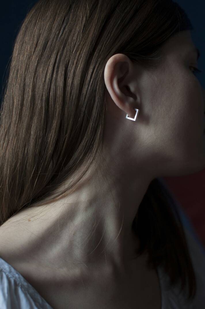 Square minimalist silver earrings on a model's ear, side view