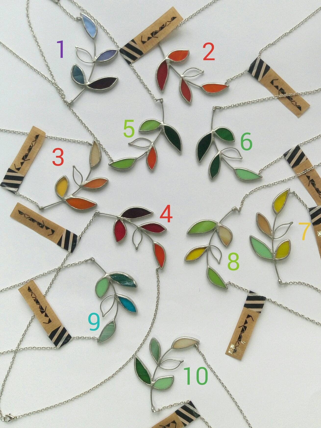 Handmade stained glass necklace with tropical leaf shapes in yellow, green, and red. Botanical nature-inspired pendant on metal chain.