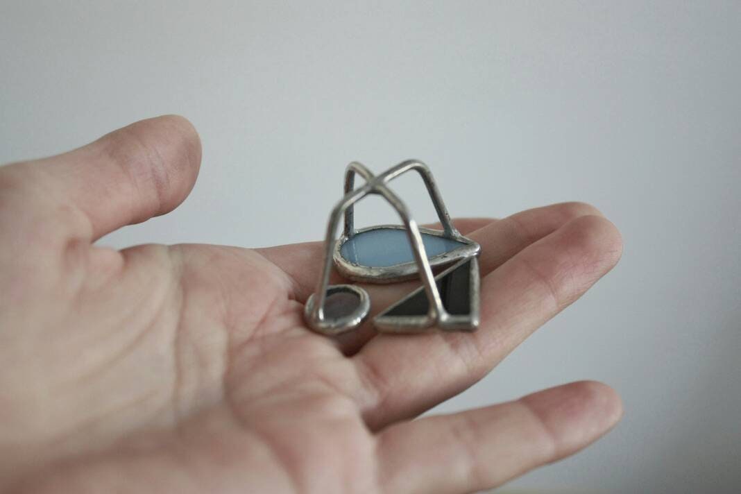Hand holding modern stained glass ring with blue teardrop and abstract shapes