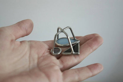 Hand holding modern stained glass ring with blue teardrop and abstract shapes