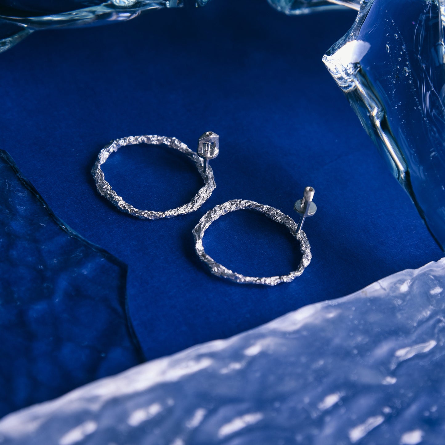 Sterling silver textured circle stud earrings on blue background with reflective glass.