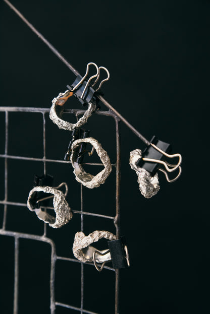 Silver crumpled rings hanging on display grid
