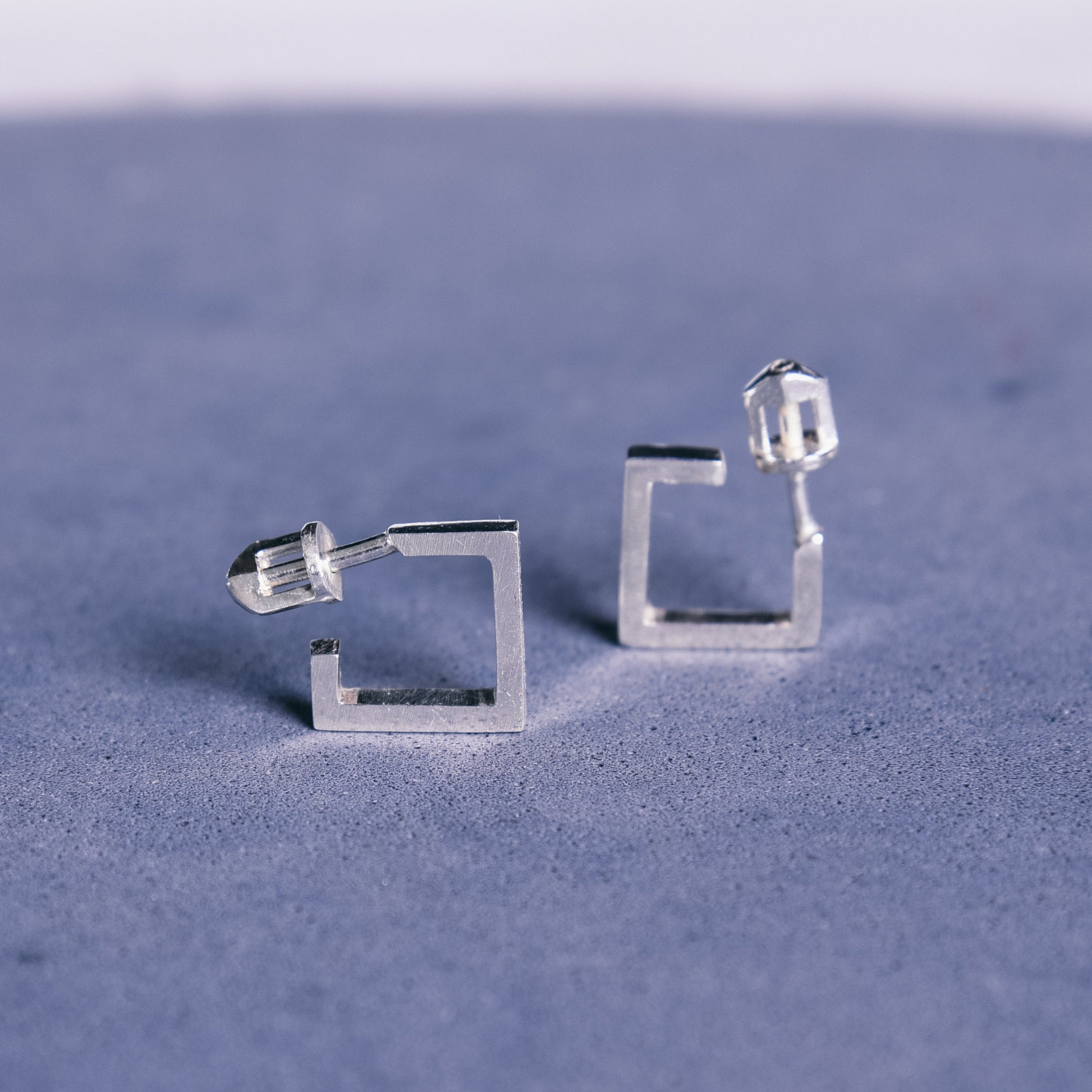 minimalist silver stud earrings on blue background