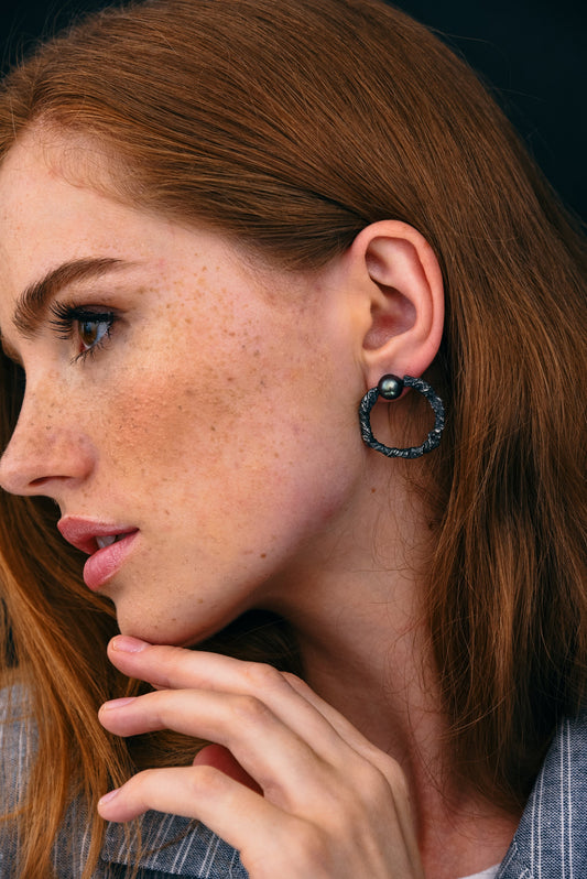 Black pearl hoop earrings worn on ear, textured sterling silver circle studs