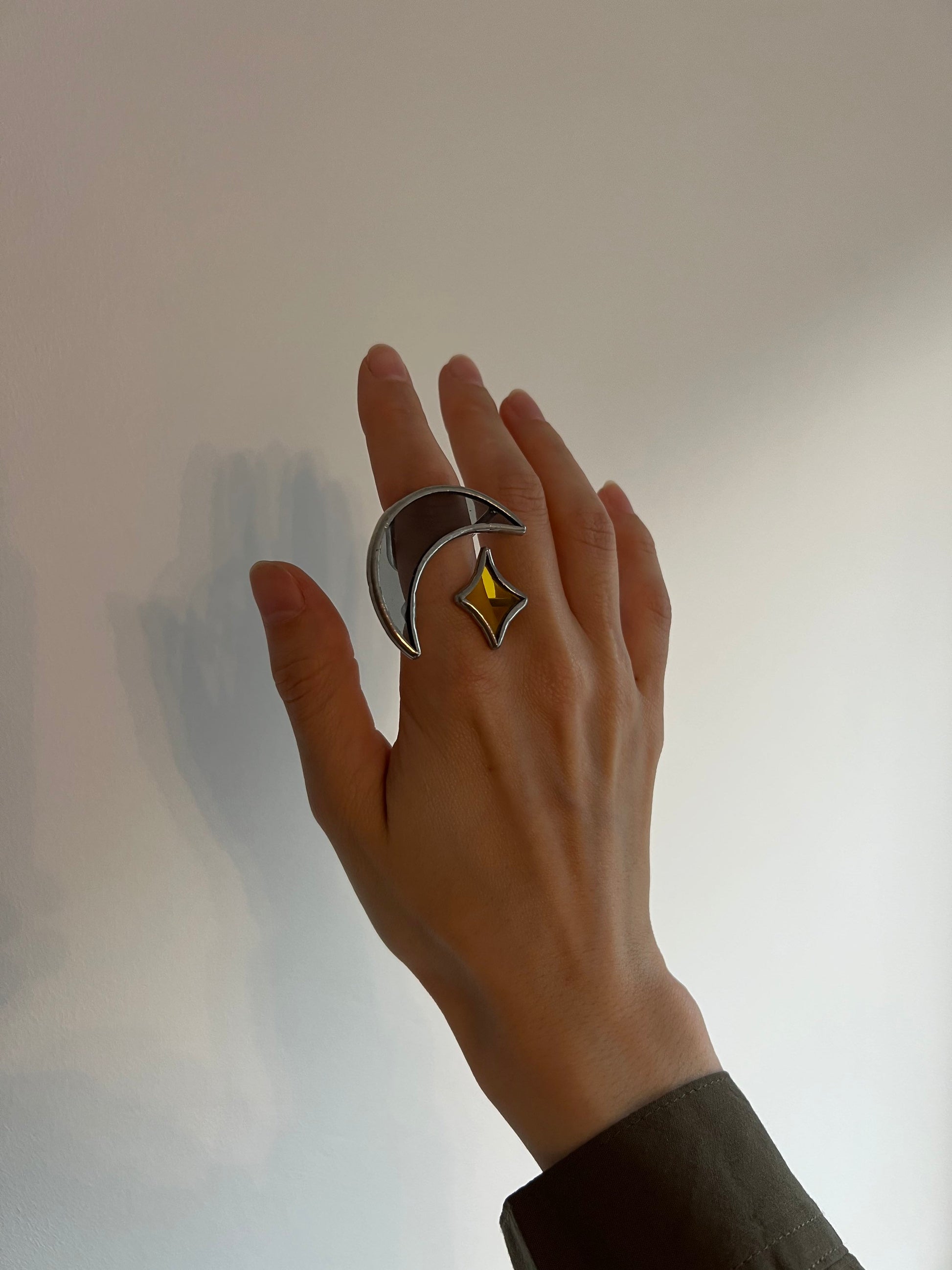 Crescent moon ring with yellow glass star shown on hand against soft grey wall