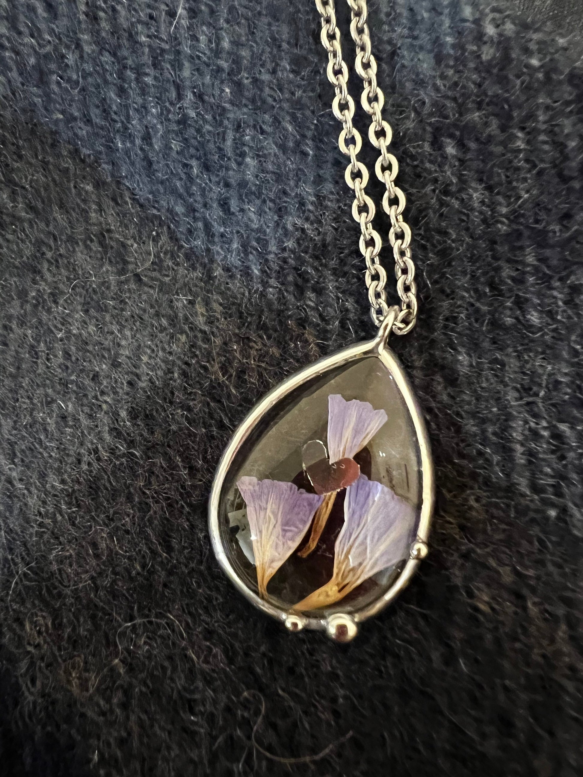 Teardrop stained glass necklace with dried purple flowers on dark fabric