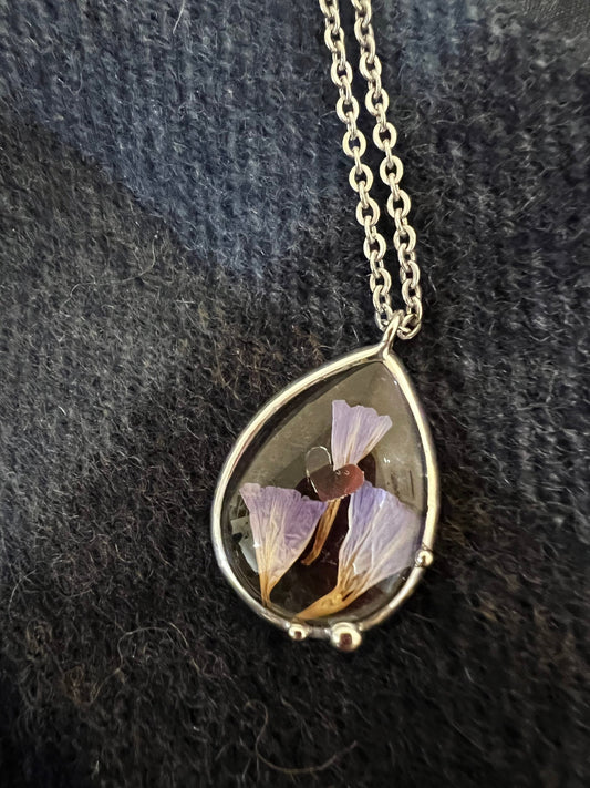 Teardrop stained glass necklace with dried purple flowers on dark fabric