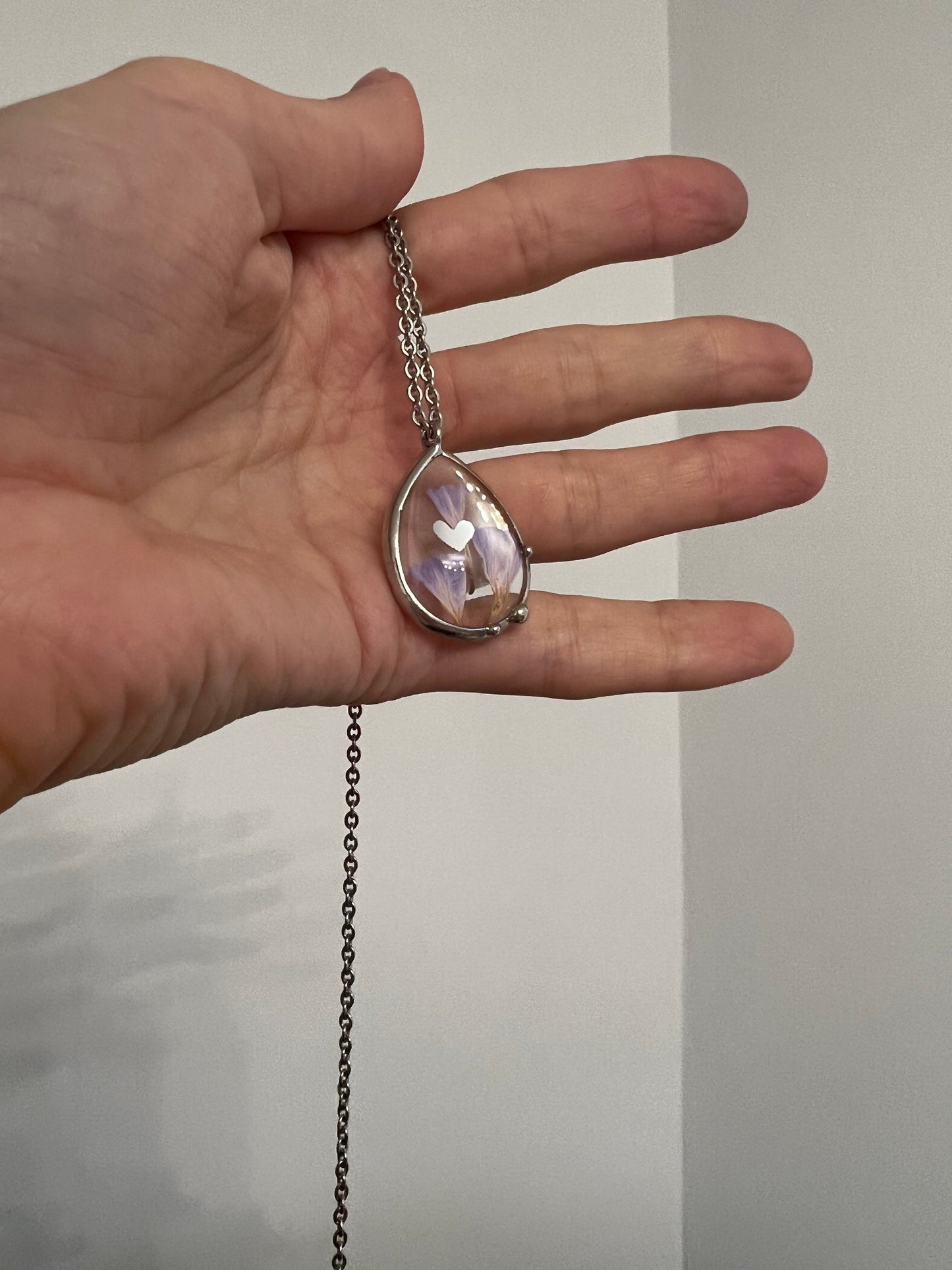 Hand holding teardrop pendant with real pressed purple flowers
