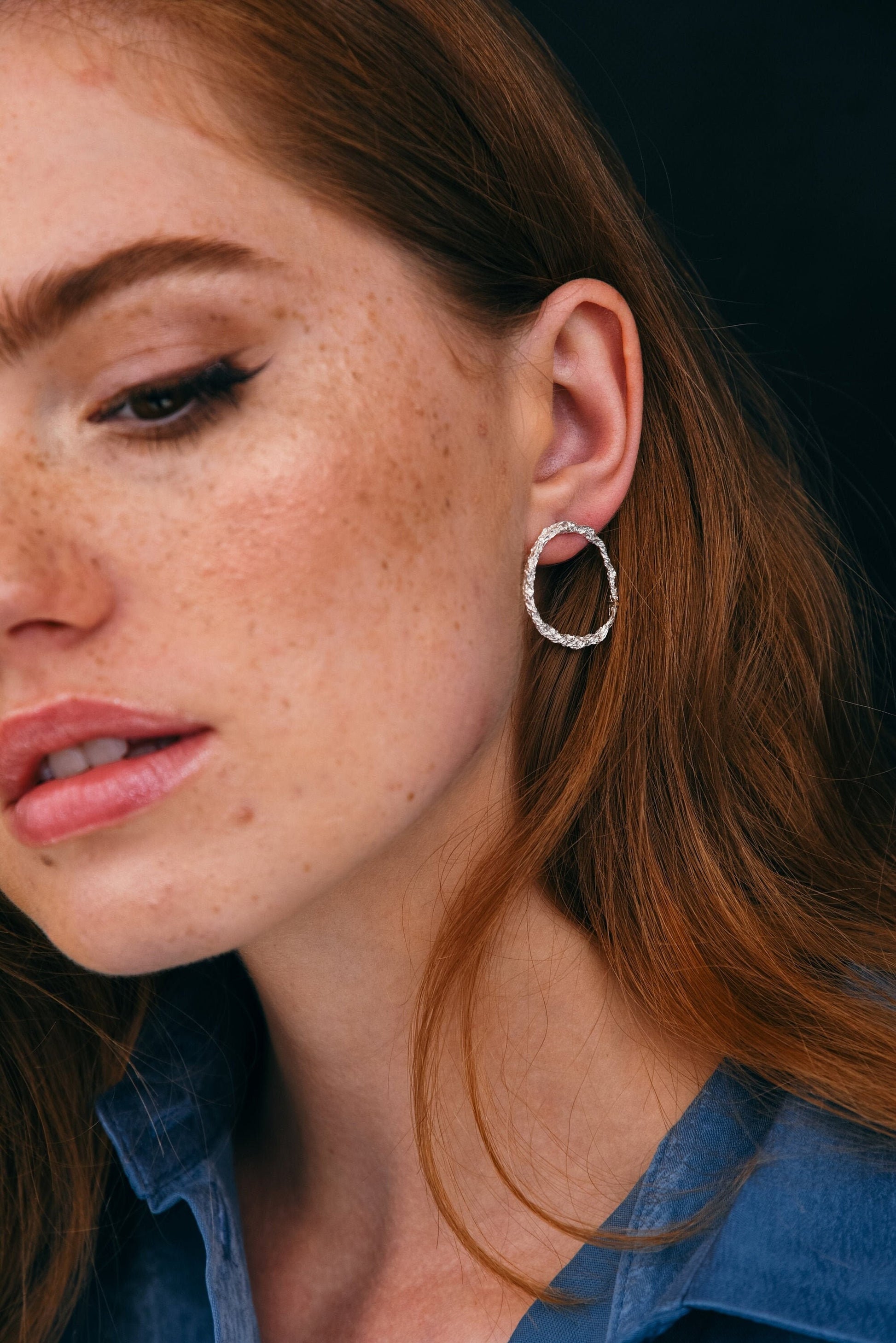Close-up portrait showing hammered silver hoop studs on red-haired model.