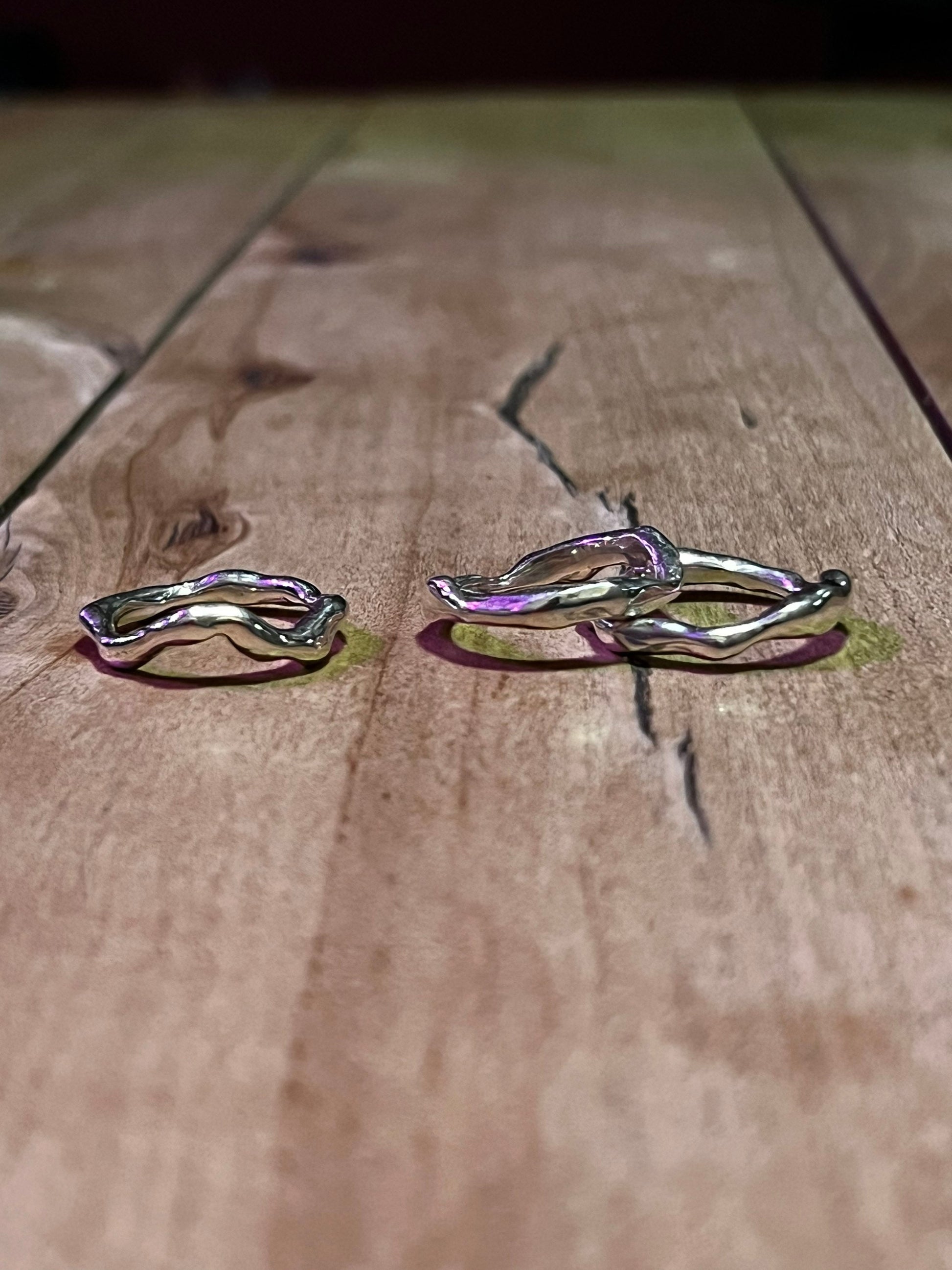 Three silver wavy rings on a wooden surface – molten wave rings set.