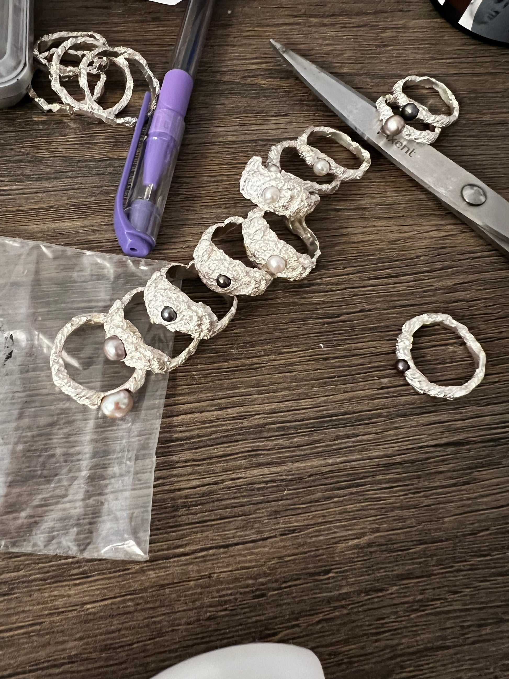 Collection of handmade sterling silver rings with pearls, artisan jewelry workspace view.