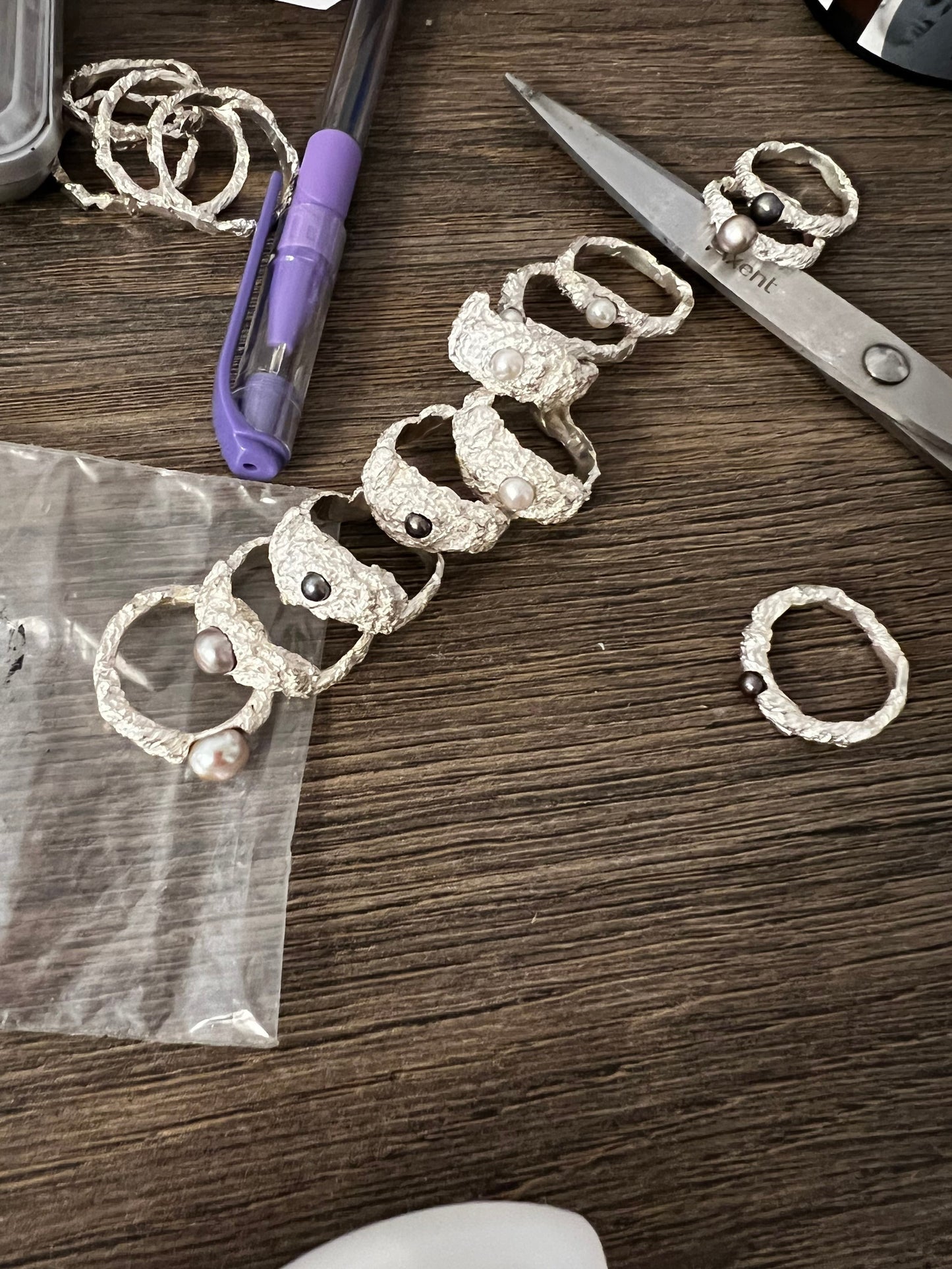 Collection of handmade sterling silver rings with pearls, artisan jewelry workspace view.