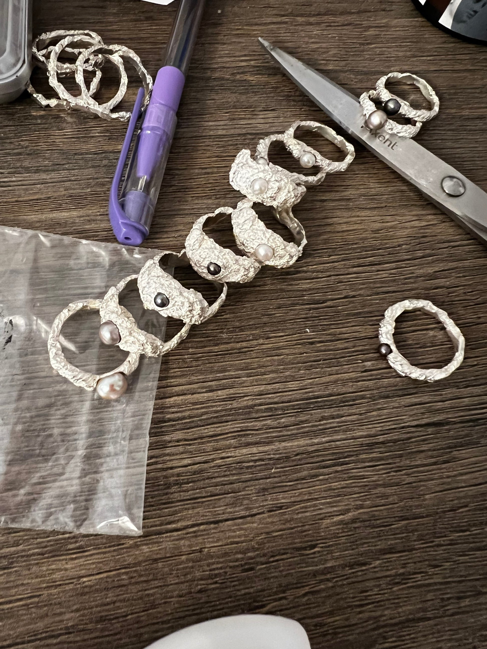 Collection of handmade sterling silver rings with pearls, artisan jewelry workspace view.