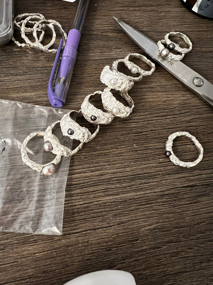 Collection of handmade sterling silver rings with pearls, artisan jewelry workspace view.
