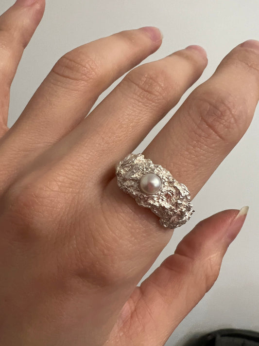 Hand wearing silver ring with white pearl, soft natural light jewelry.