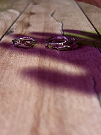 Three silver rings in wavy style on a wooden surface.