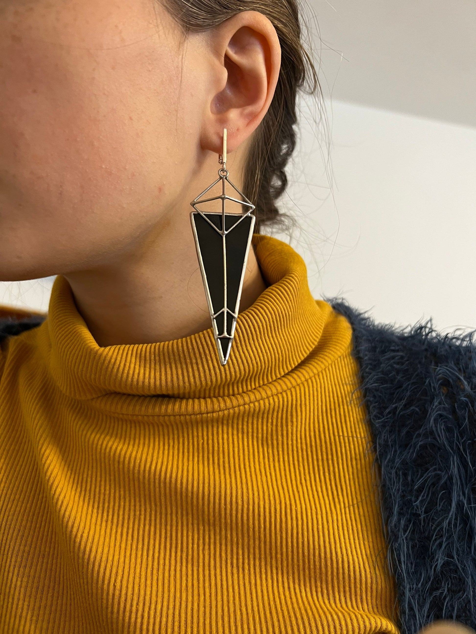 Large statement earrings in the shape of a pyramid on a model in a yellow sweater