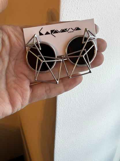 Handmade black geometric stud earrings shown in hand for scale