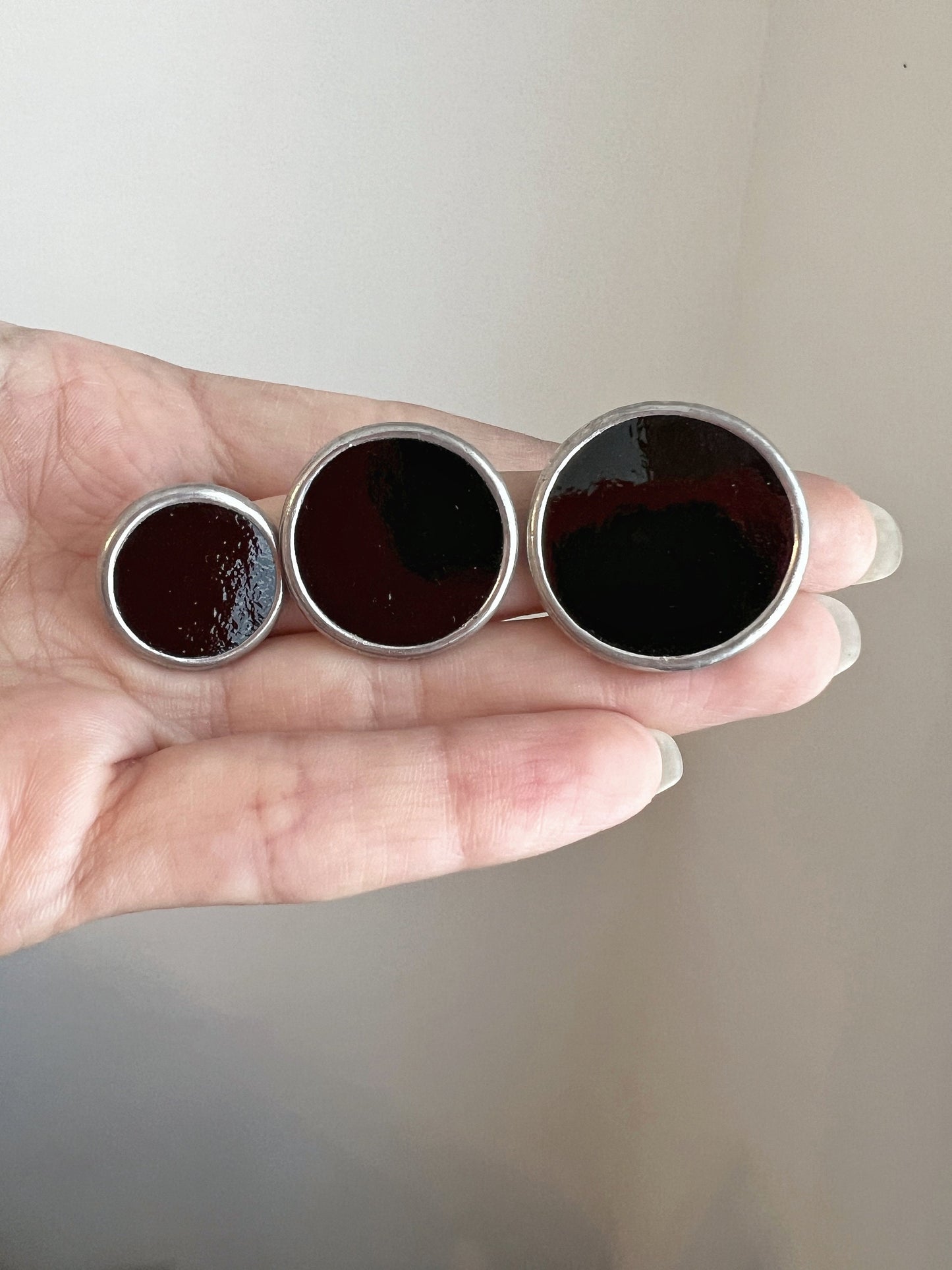 Handmade black glass round stud earrings size comparison in hand