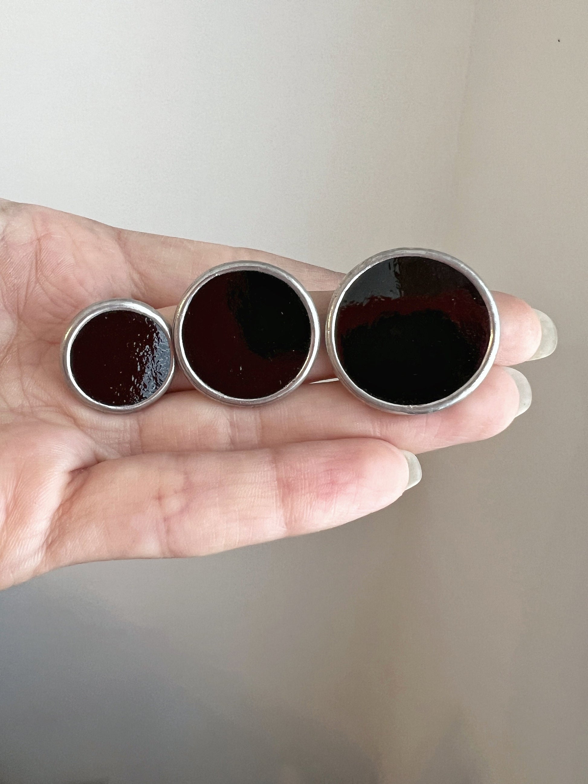Handmade black glass round stud earrings size comparison in hand
