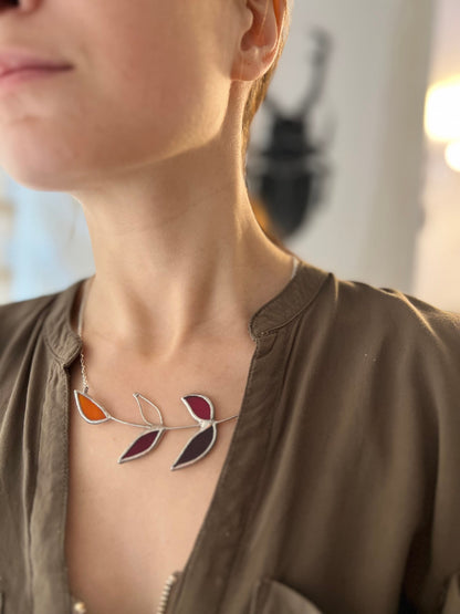 Minimalist pendant with red and wine leaf shapes, stained glass on silver branch form — nature-inspired fall jewelry.