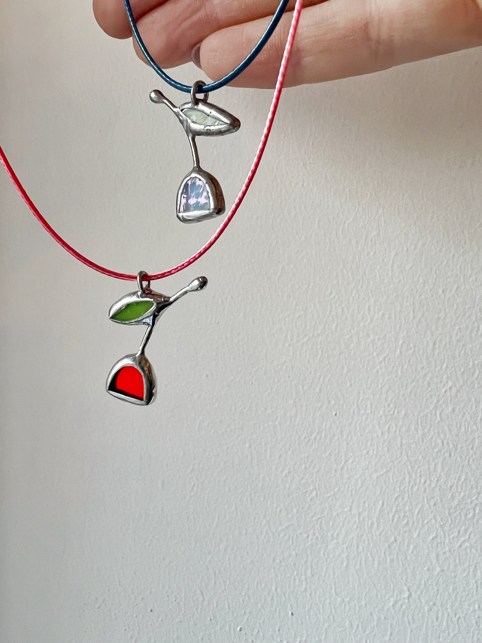 Small handmade stained glass tulip pendant in red tones with silver edge, hanging on a necklace, worn close to collarbone