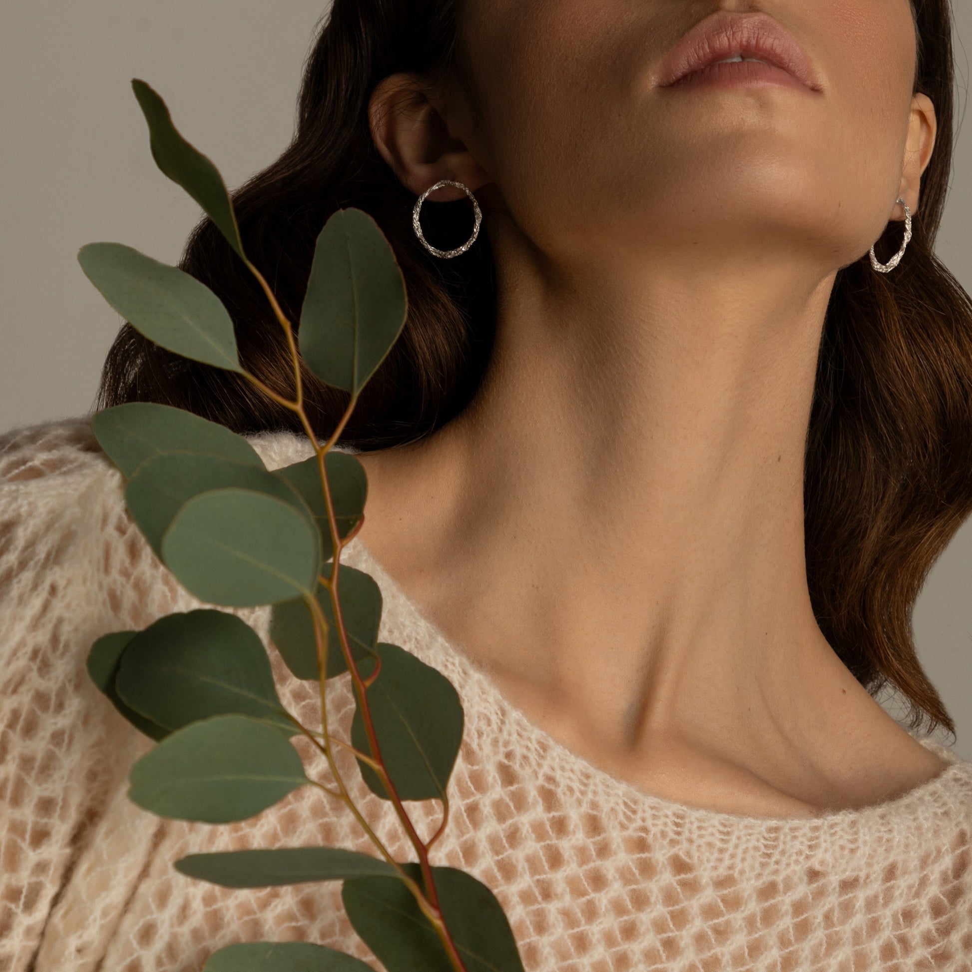 Textured silver hoop studs styled with natural greenery branch.