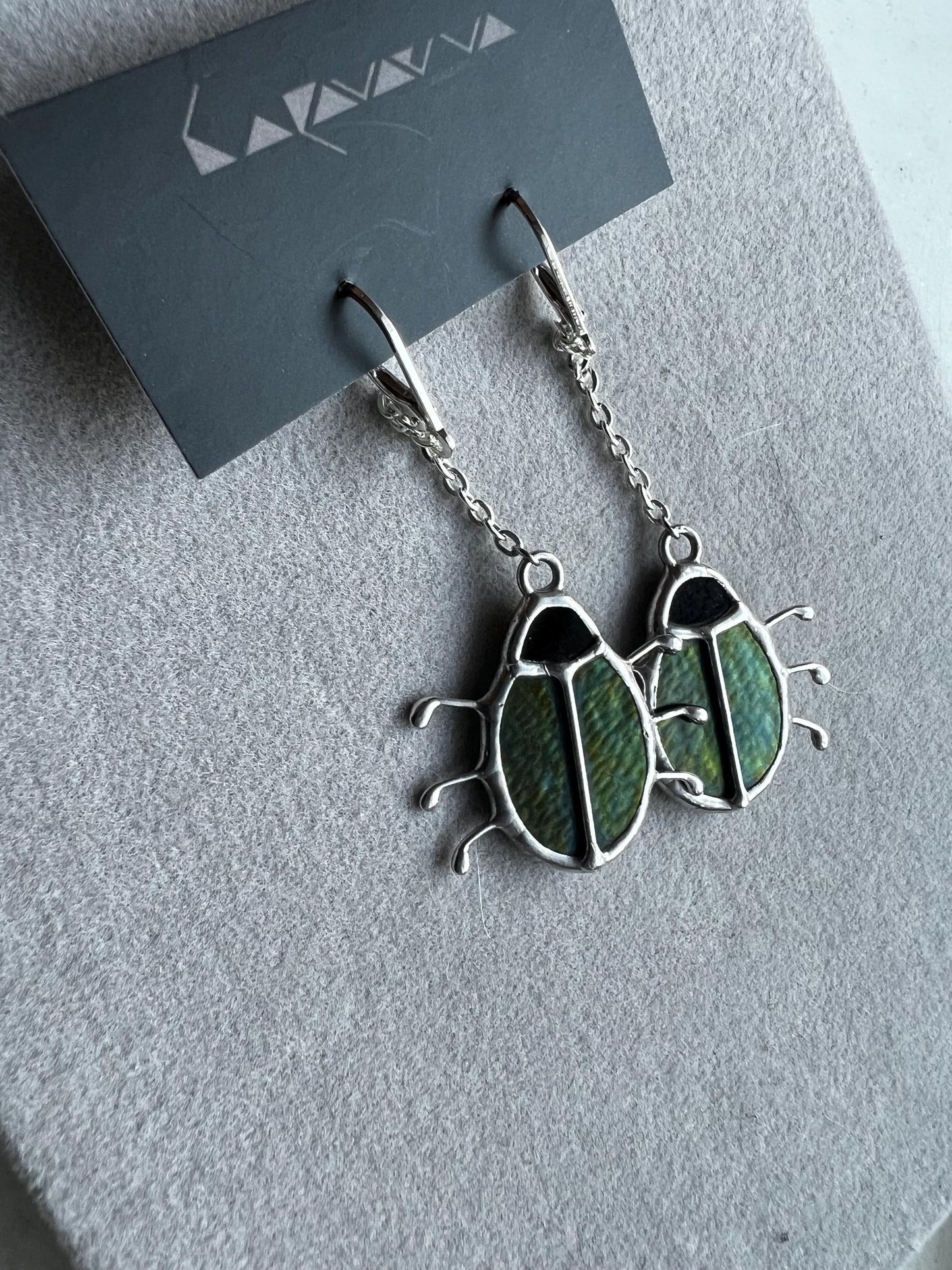 Stained glass insect earrings on grey background, green iridescent beetles