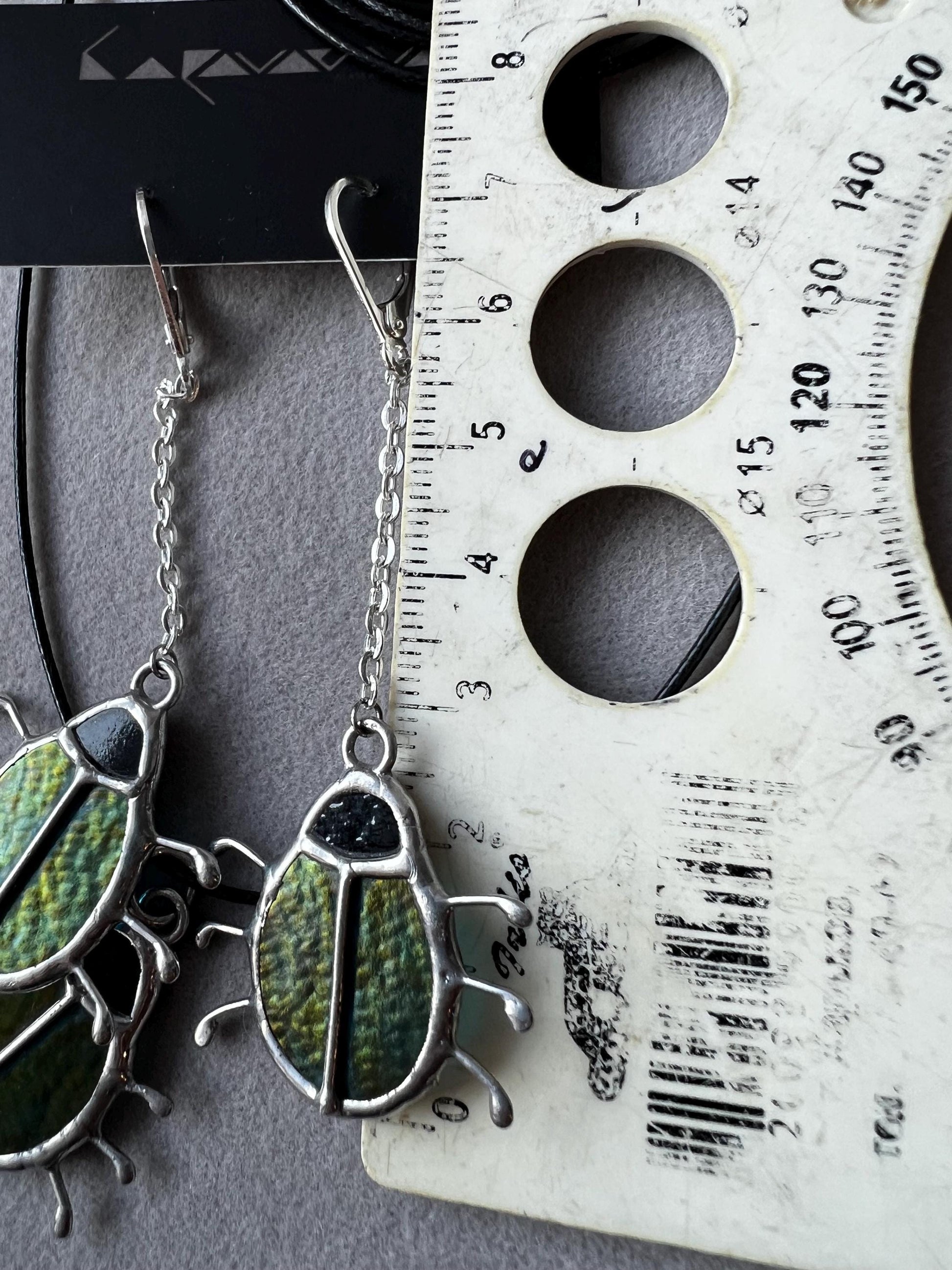 Close-up of green stained glass beetle earrings, handmade insect design
