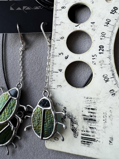 Close-up of green stained glass beetle earrings, handmade insect design