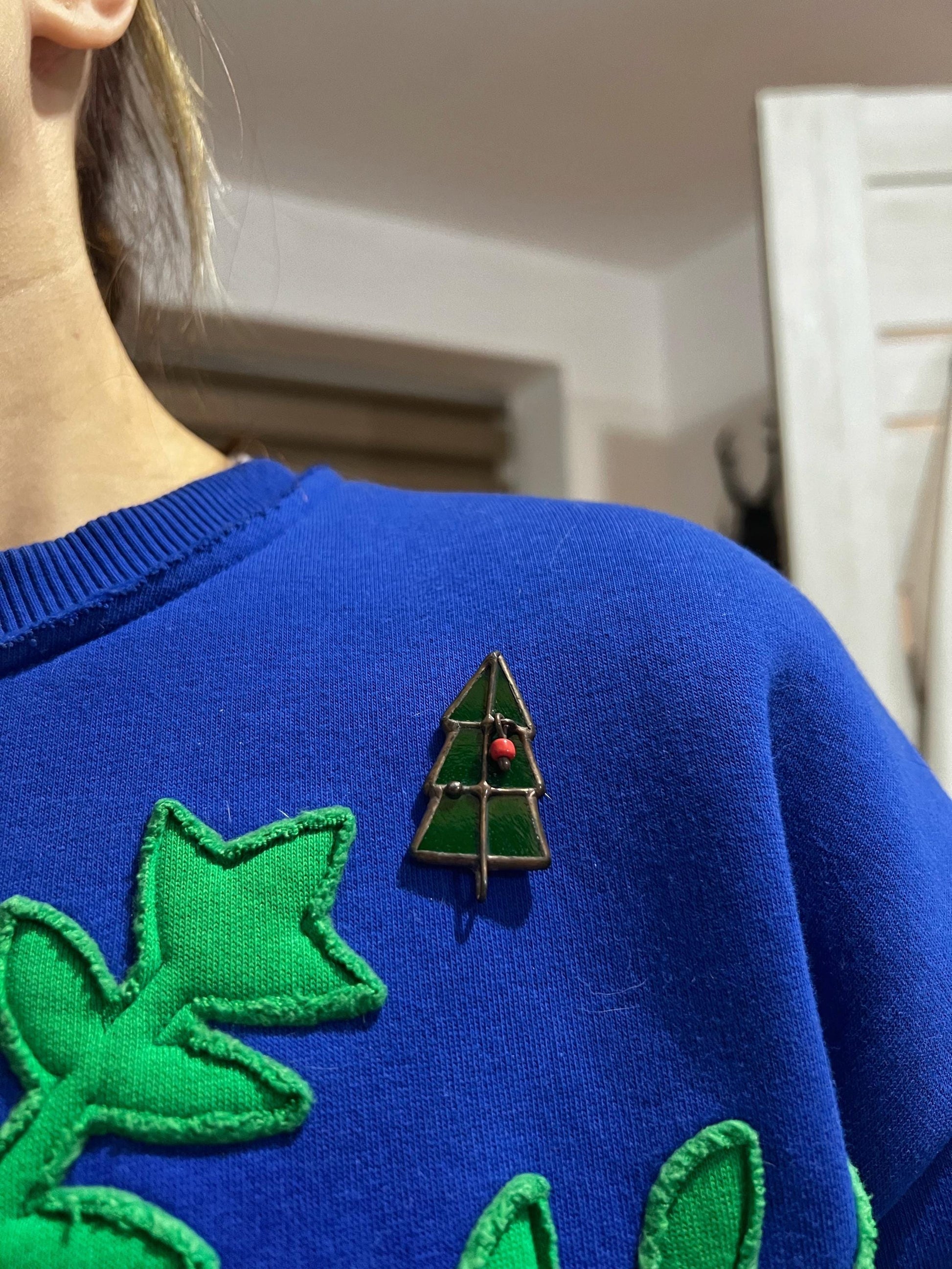 Green Christmas tree brooch attached to a blue sweater