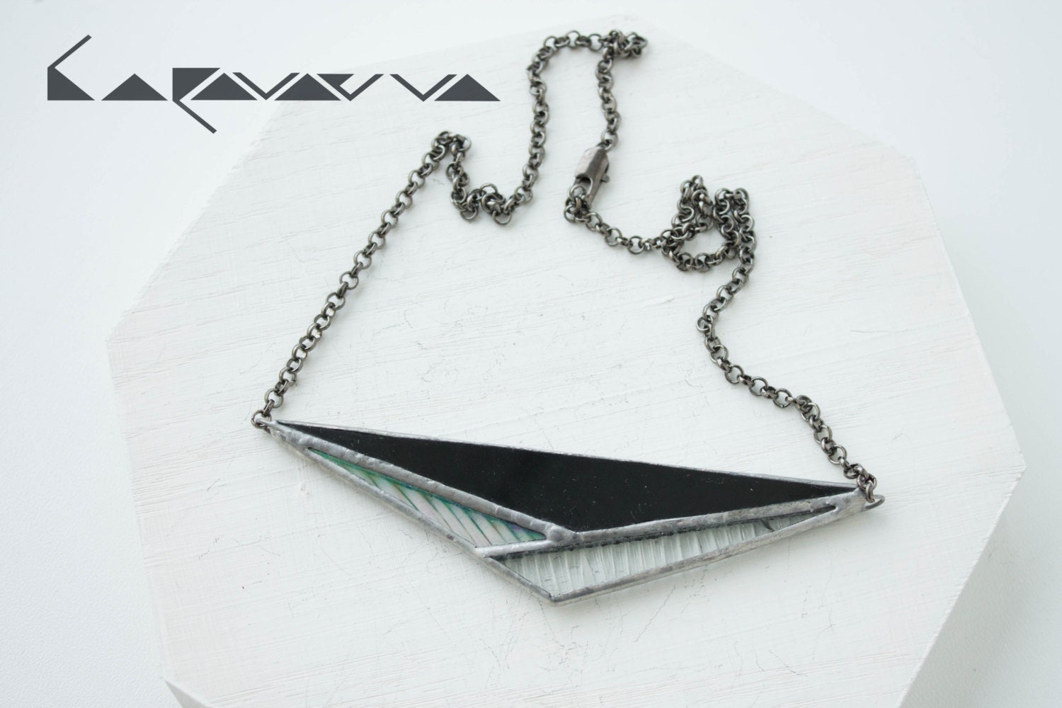 A close-up of the pendant on a white background - a geometric triangle made of glass, a contrast of black and transparent.