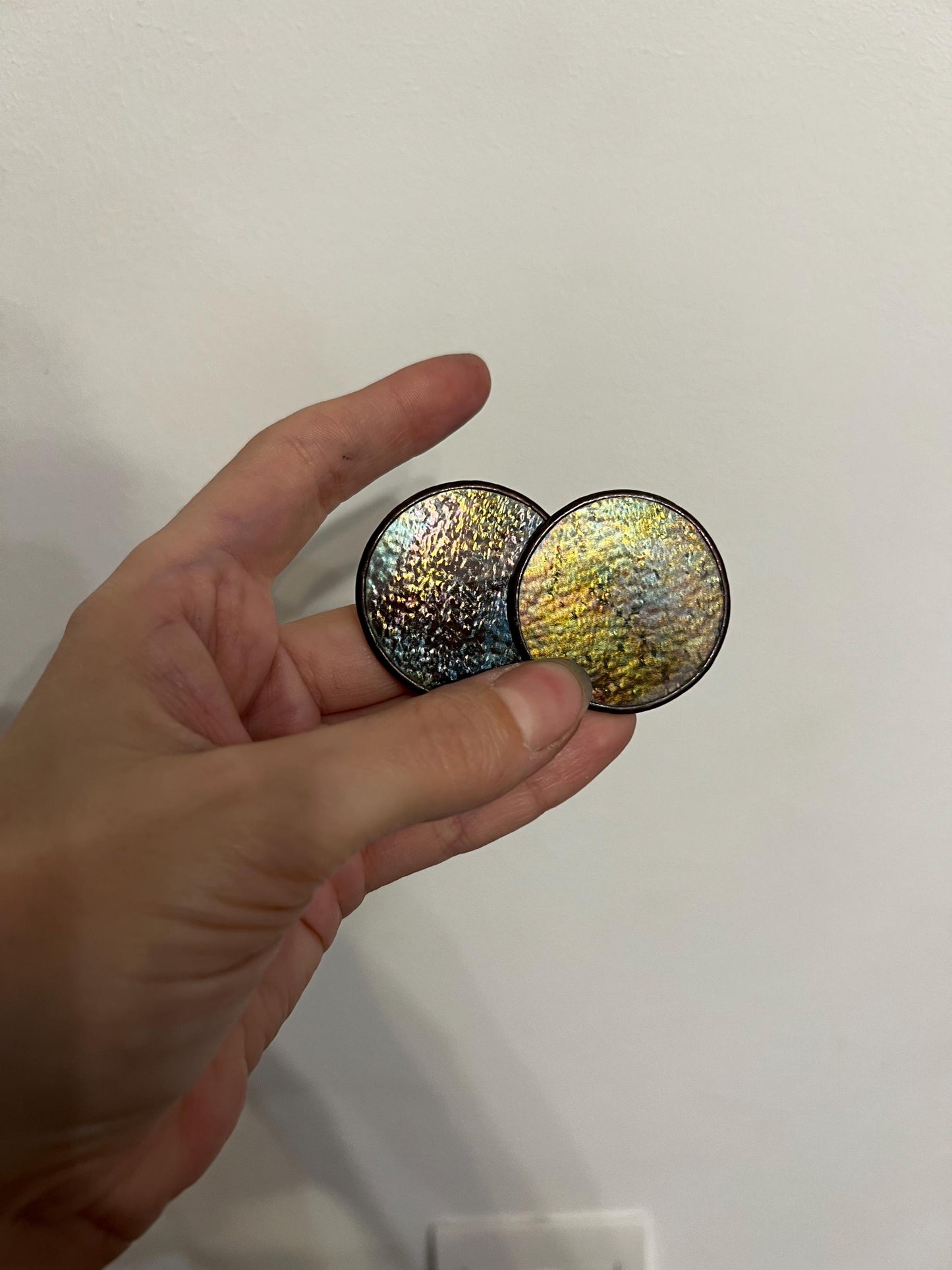 black iridescent stained glass earrings discs in hand close-up well depict the iridescence of the glass