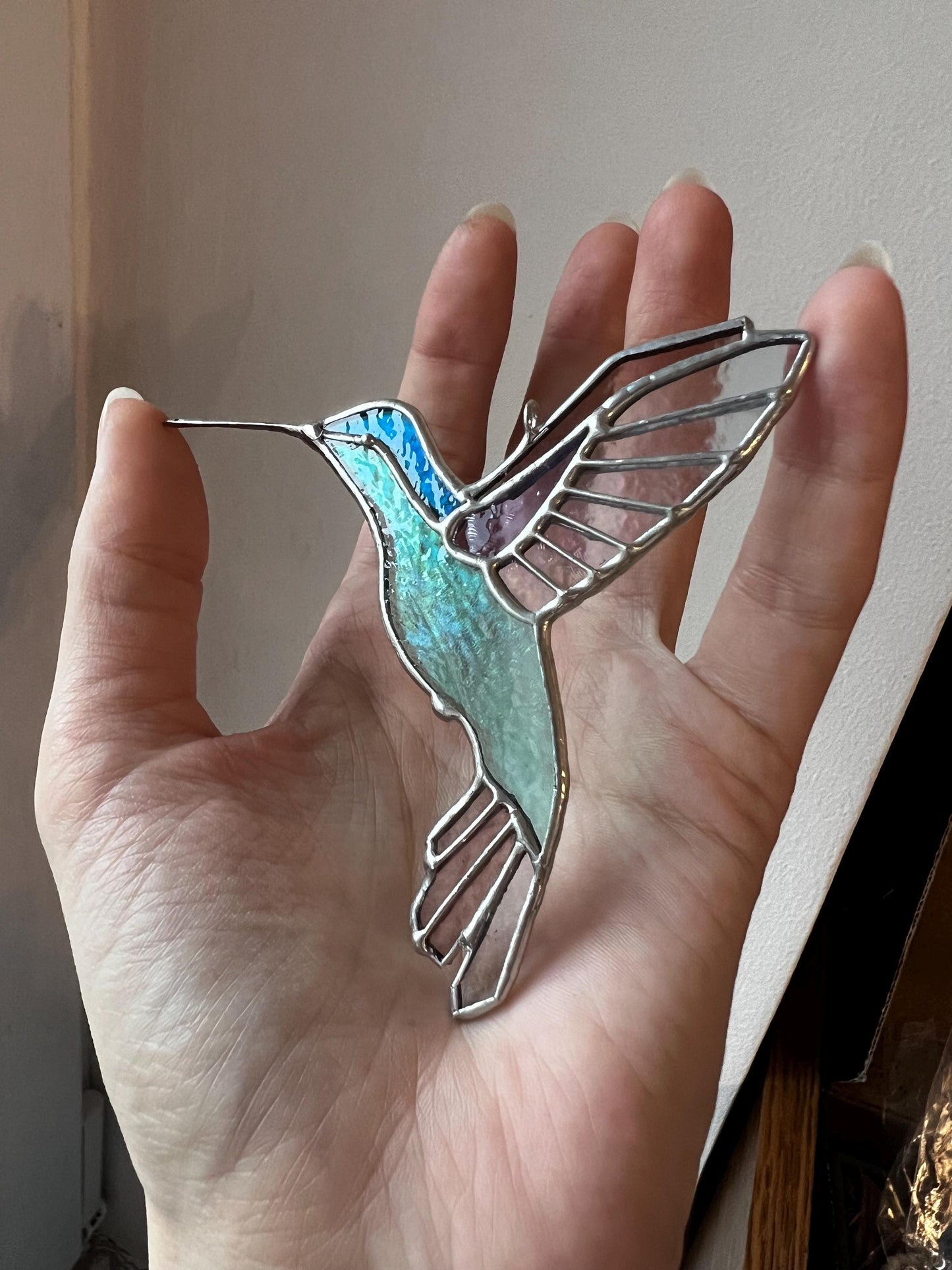 Light iridescent blue stained glass hummingbird suncatcher in hand, handmade bird ornament