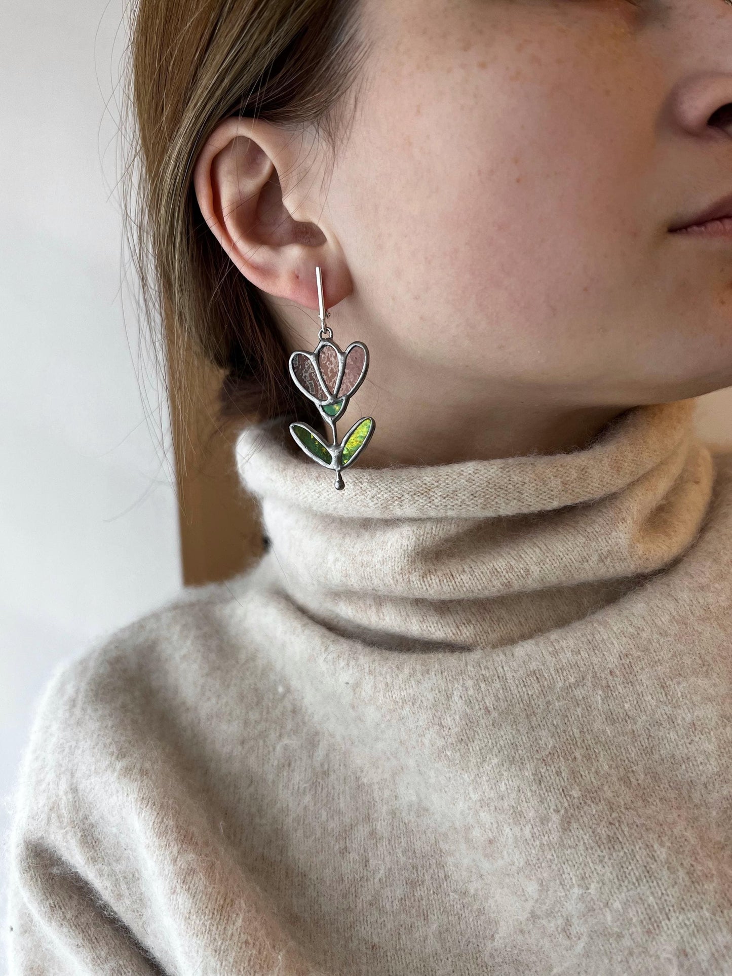 Woman wearing plum stained glass flower earrings with green leaves.