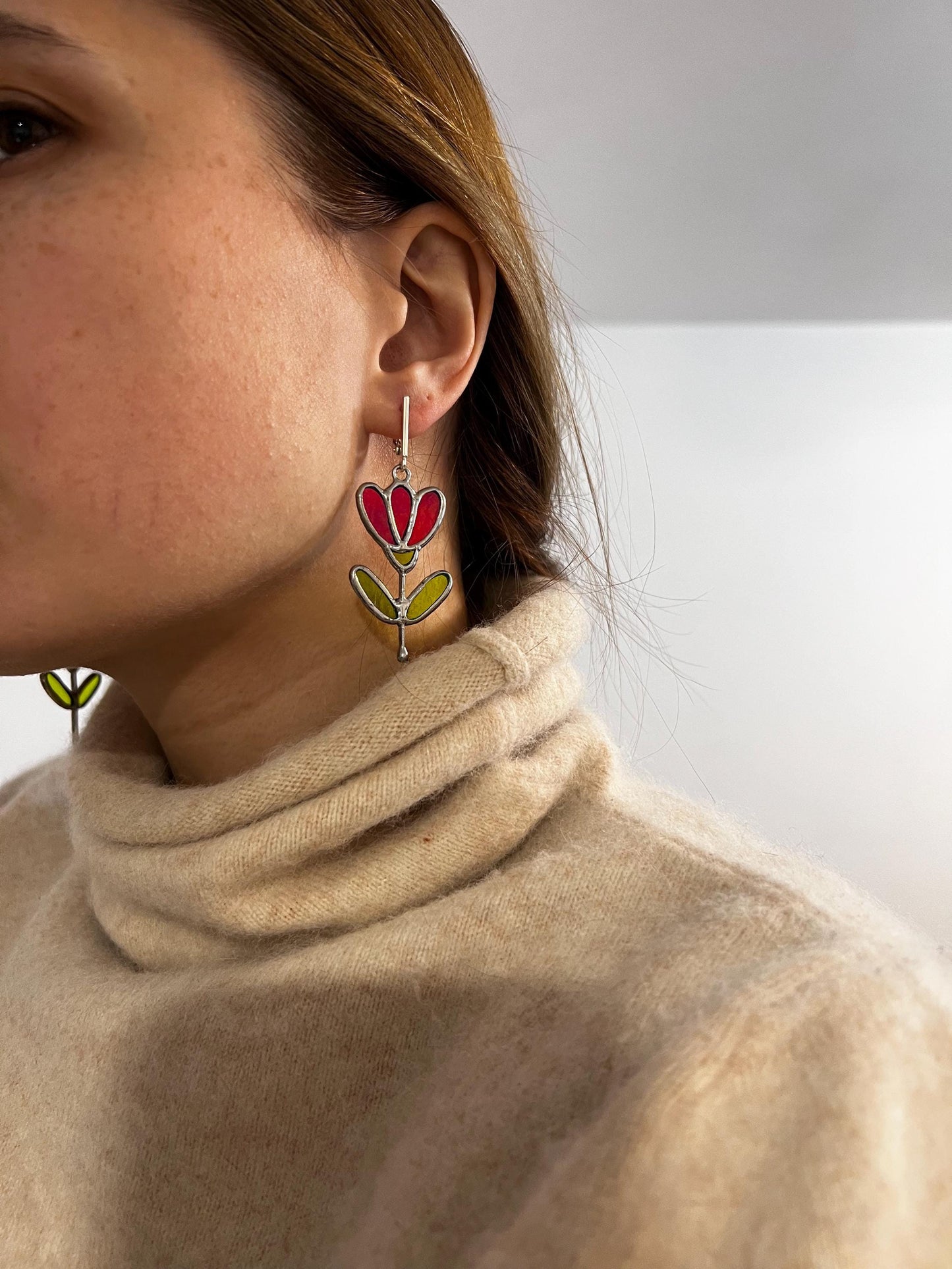 Model wearing red stained glass flower earrings with green leaves.