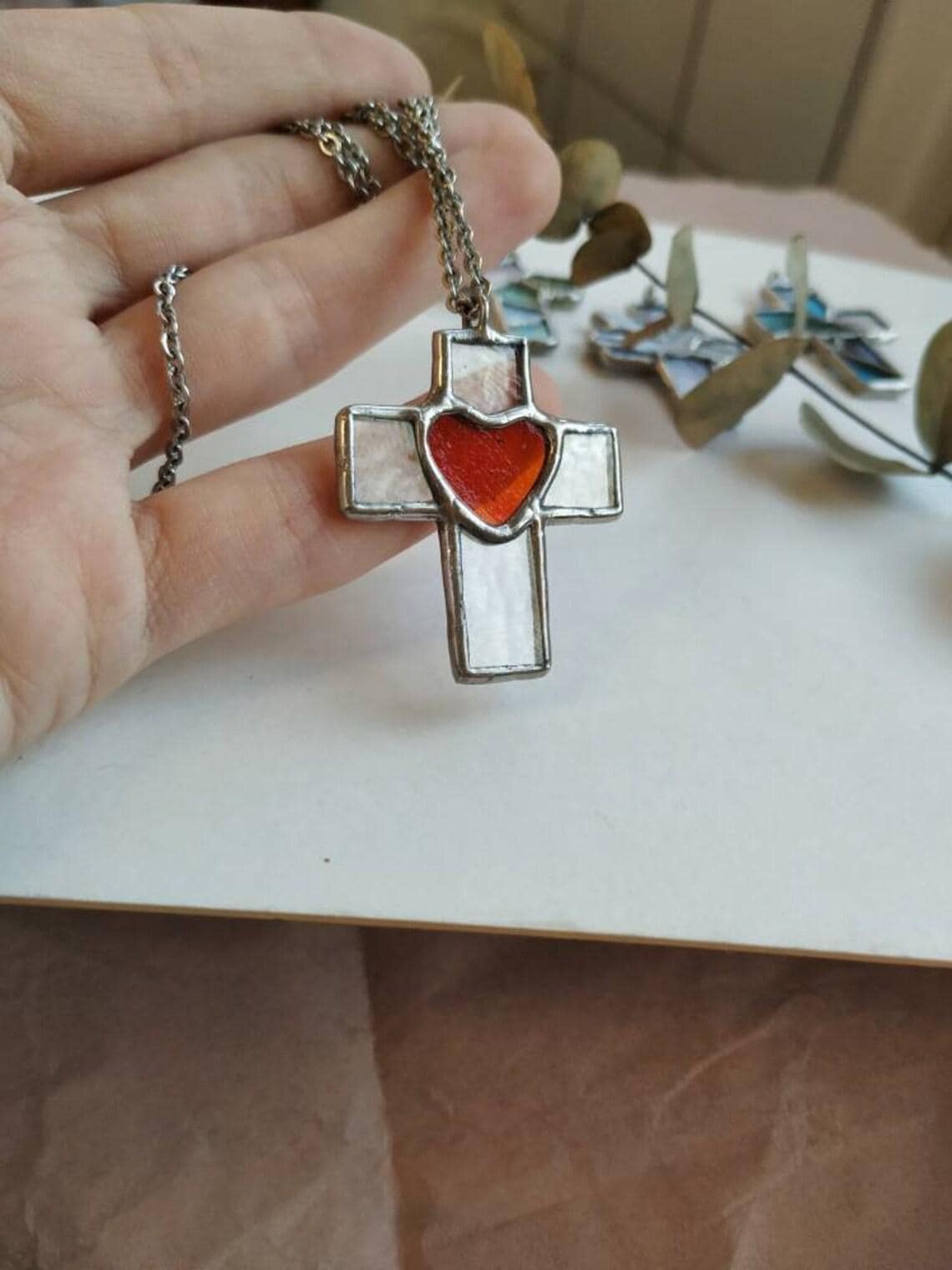 Hand holding chunky cross pendant with red heart detail