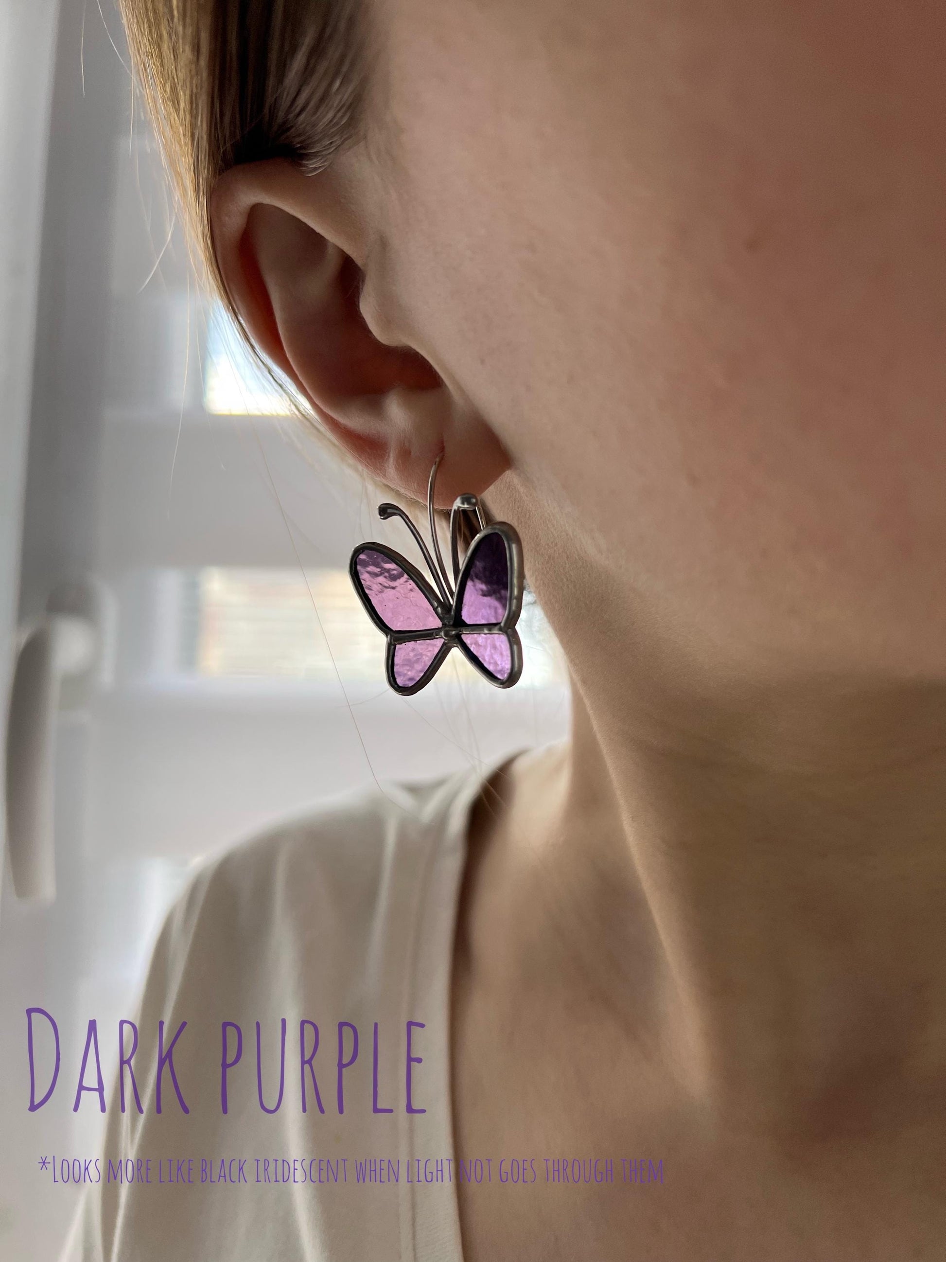 Close-up of woman wearing dark purple stained glass butterfly dangle earrings