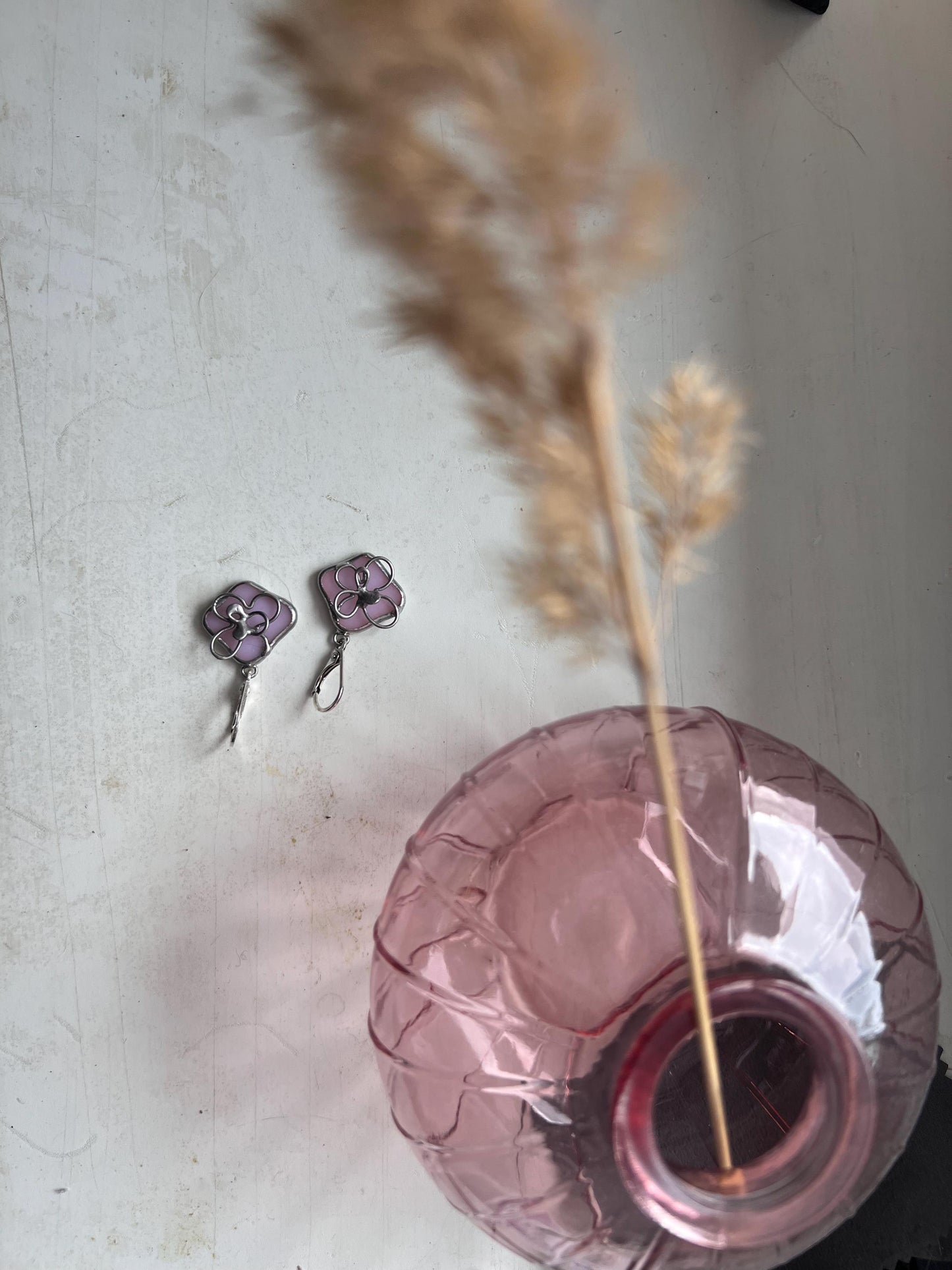 Sakura stained glass earrings lying on table beside glass vase, pink cherry blossom jewelry flatlay
