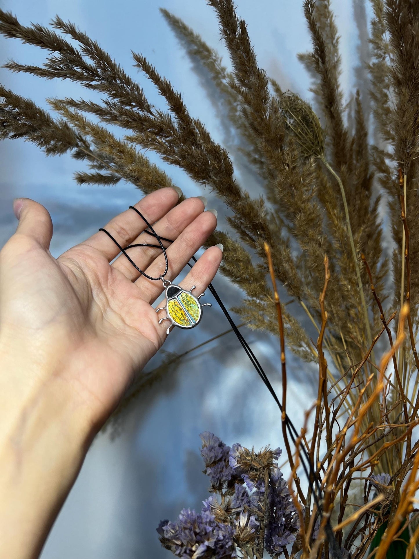 Hand holding stained glass green bug pendant with iridescent shine