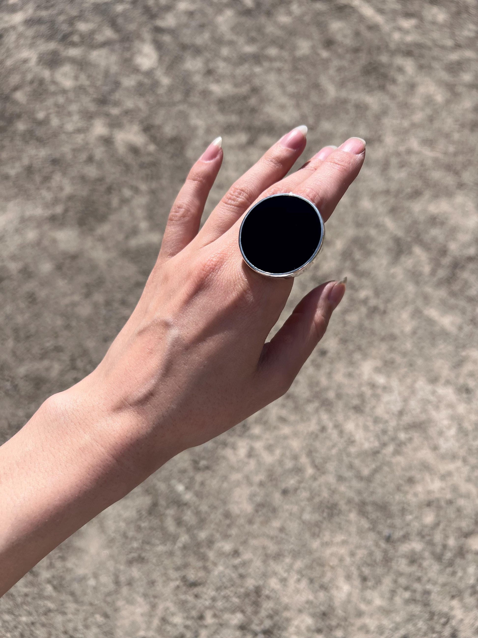 Black opal glass ring on hand, chunky round sterling silver statement ring outdoors