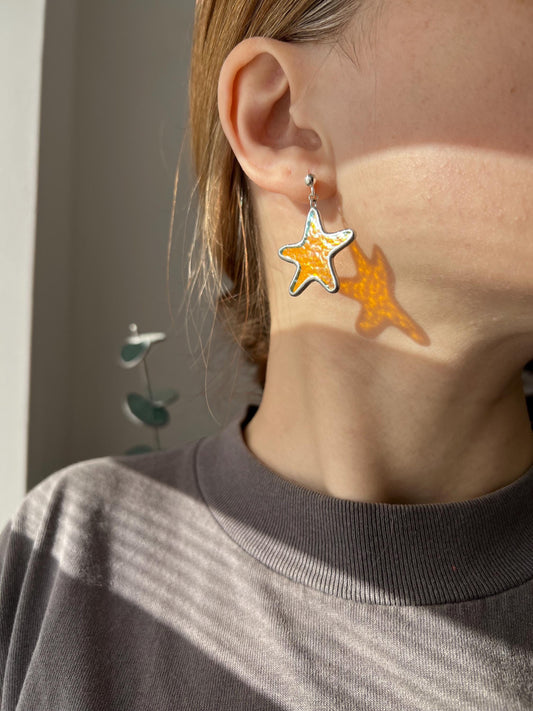 Yellow stained glass starfish earrings worn on ear in sunlight